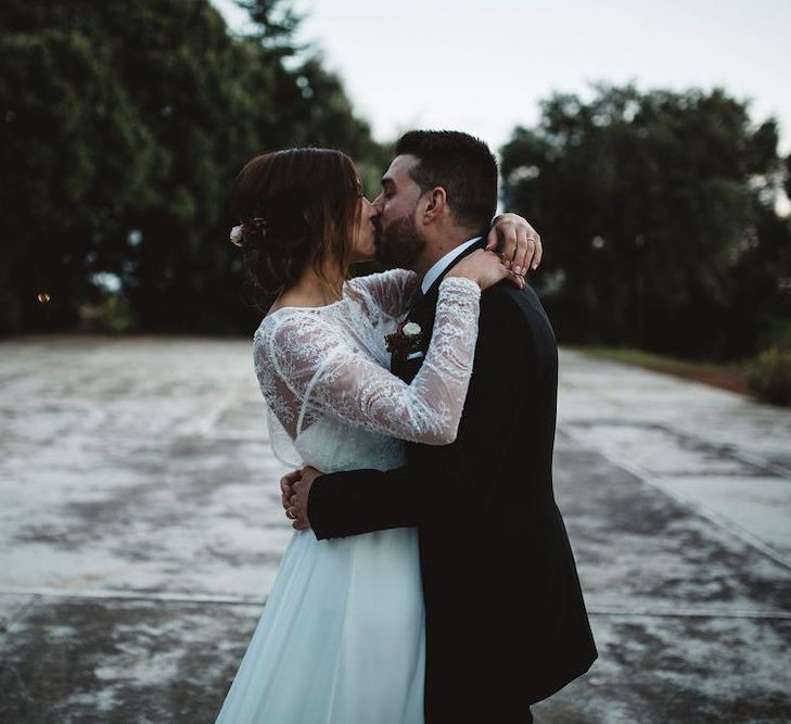 Bride in Jordi Anguera Wedding Dress with Lace Overlay and Groom in Señor Suit Kissing