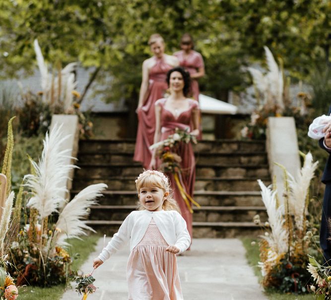 Flower girl walking down the aisle in a pink dress and white cardigan