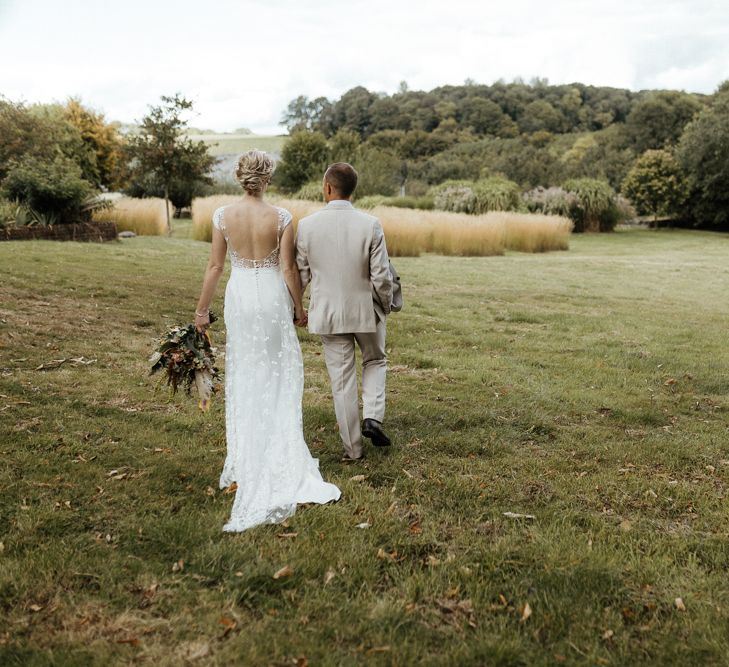 Bride in Rime Arodaky wedding dress and groom in stone suit walking through the fields