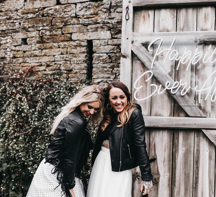 Same-sex brides standing next to a neon sign