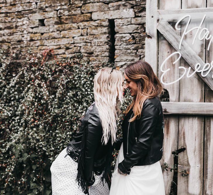 Rock n Roll brides in leather jackets standing next to a neon sign