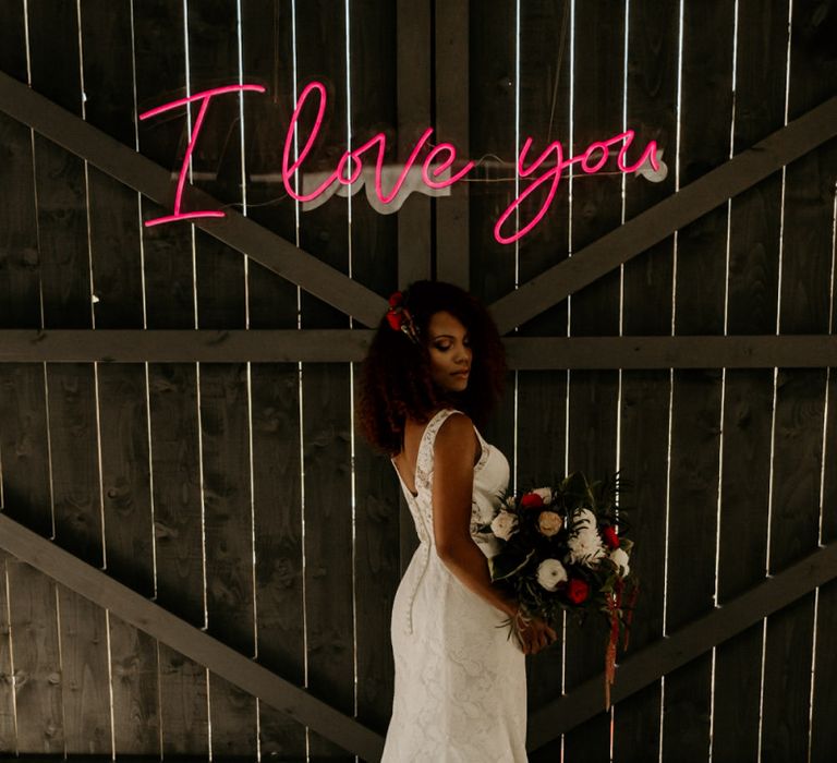 Black Bride with Afro Hair in Lace Wedding Dress Holding a Red and White Wedding Bouquet Under a Neon Wedding sign