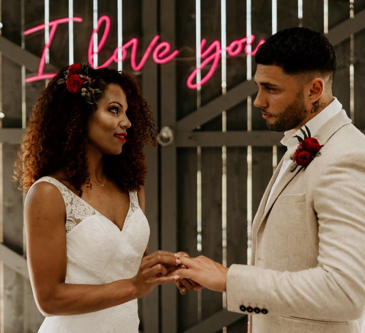 Black Bride with Afro Hair in a Lace Wedding Dress and Groom in Blazer Exchanging Vows Under a Neon Wedding Sign