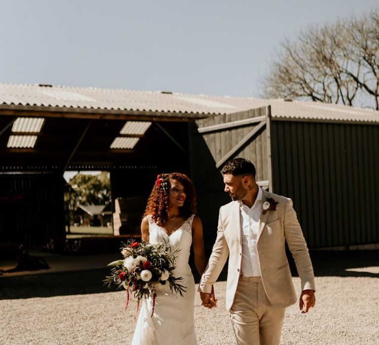 Black Bride with Afro Hair in a Lace Wedding Dress and Groom in Blazer Holding Hands