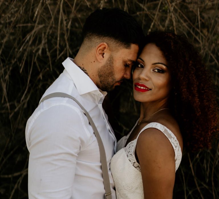 Black Bride with Afro Hair in a Lace Wedding Dress and Groom in White Shirt and Braces Embracing