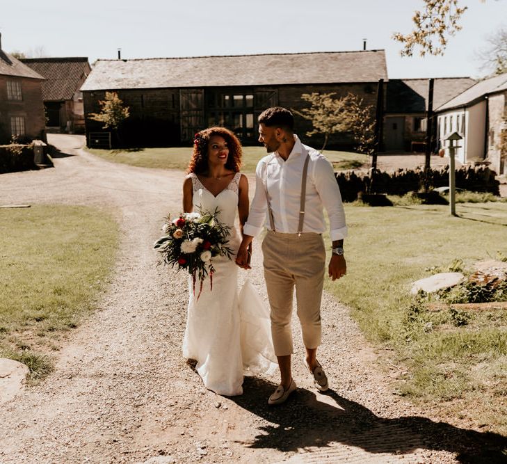 Black Bride with Afro Hair in a Lace Wedding Dress and Groom in White Shirt and Braces Walking Through the Barn