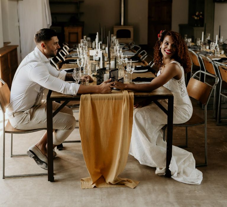 Black Bride in Lace Wedding Dress Holding Hands with Her Groom Across The  Table