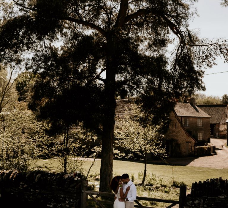 Black Bride in Lace Wedding Dress and Groom in White Shirt and Trousers Embracing in the Field