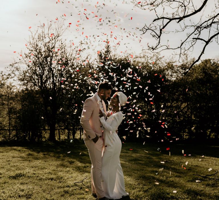 Confetti Moment with Black Bride in White Jumpsuit with Head Wrap  and Groom in Pink Suit