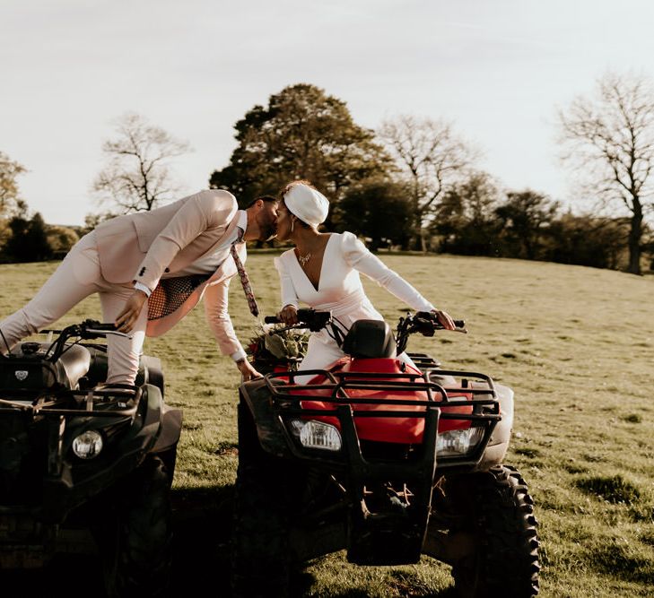 Black Bride in White Jumpsuit with Head Wrap  and Groom in Pink Suit on Quad Bikes