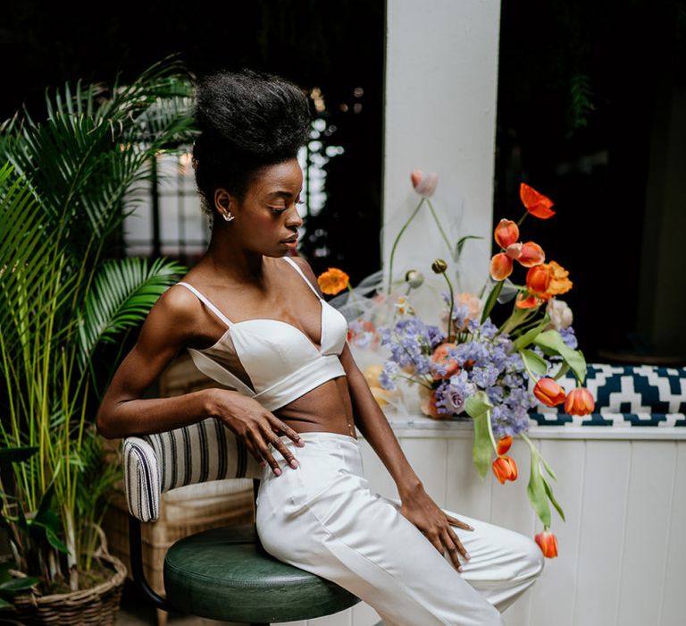 Black bride in trouser outfit surrounded by colourful spring wedding flowers