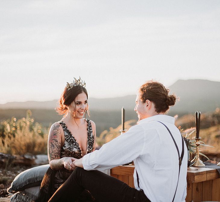 Bride in Black Wedding Dress and Gold Crown Headdress Laughing with Her Groom in White Shirt and Braces