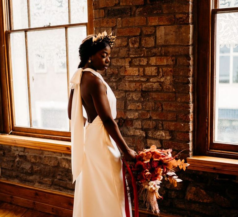 Bride holding a backless, halter neck wedding dress with caramel, raspberry and rust wedding theme bouquet