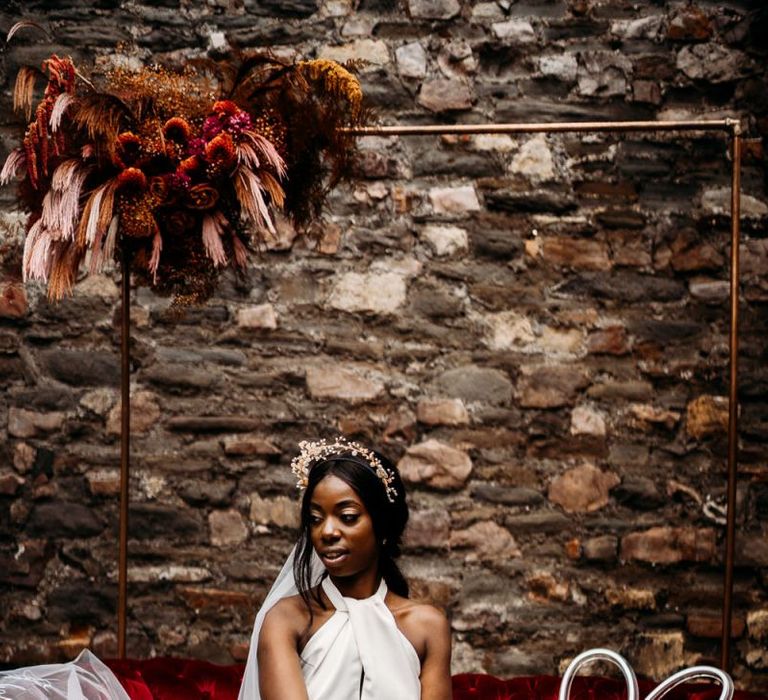 Bride sitting on a red velvet sofa in a Halfpenny London wedding dress