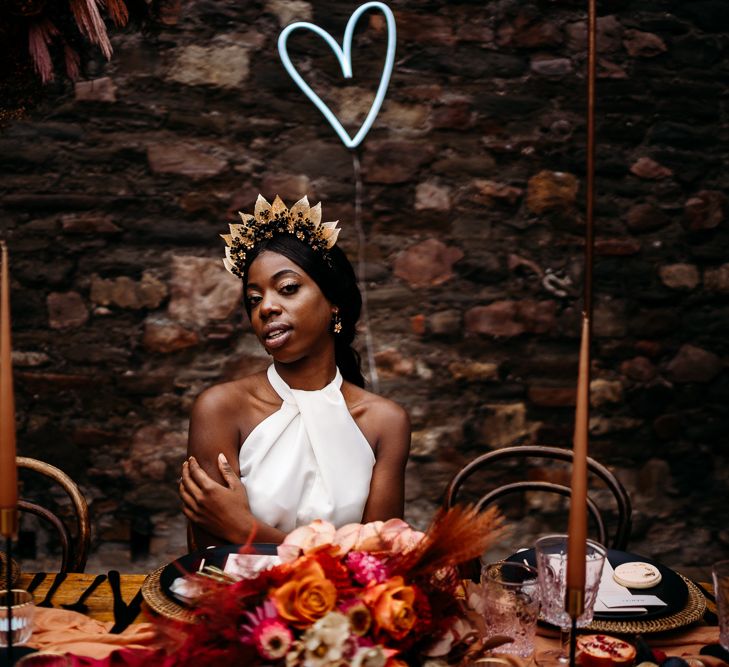 Bride sitting at a bohemian luxury tablescape with heart neon sign