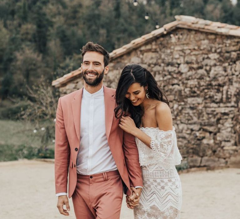 Bride in off the shoulder Grace Loves Lace Dress with groom in Coral Suit