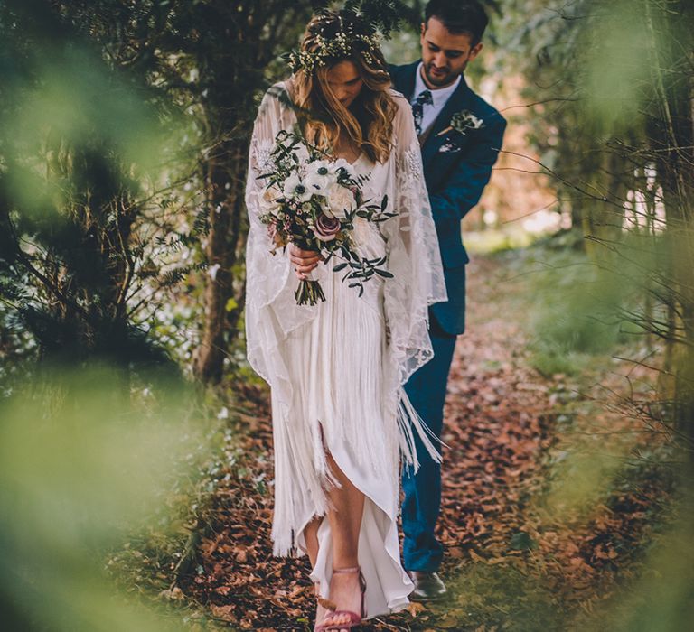 Bride and groom walking through the trees in boho wedding dress