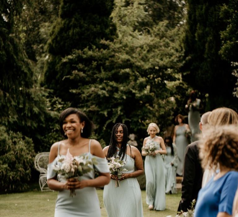 Bridesmaids in pale green dresses walking down the aisle