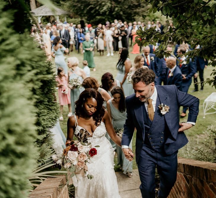 Black bride in Riki Dalal wedding dress and Irish groom in navy suit holding hands