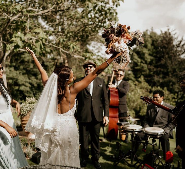 Black bride in low back Riki Dalal wedding dress and veil raising her hands in celebration