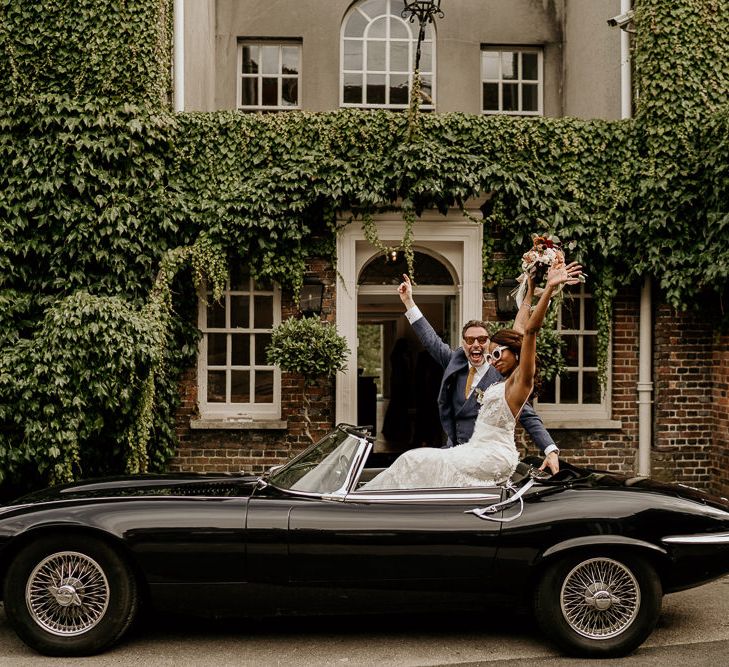 Nigerian bride and Irish groom sitting on top of a convertible E-Type Jaguar wedding car