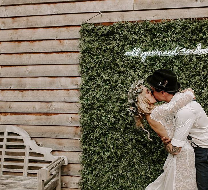 bride and groom kiss in front of foliage backdrop and neon sign