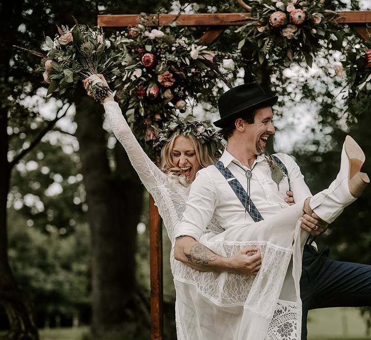 Groom plays guitar on brides leg who clutches Protea bouquet and wears bridal boots