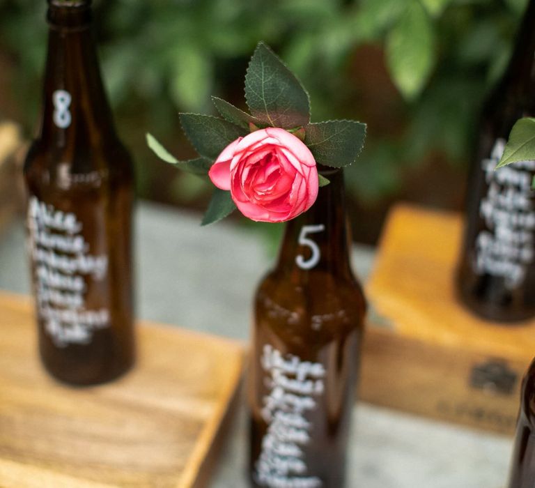 Bright pink peony resting inside brown beer bottle as part of a DIY bottle table plan