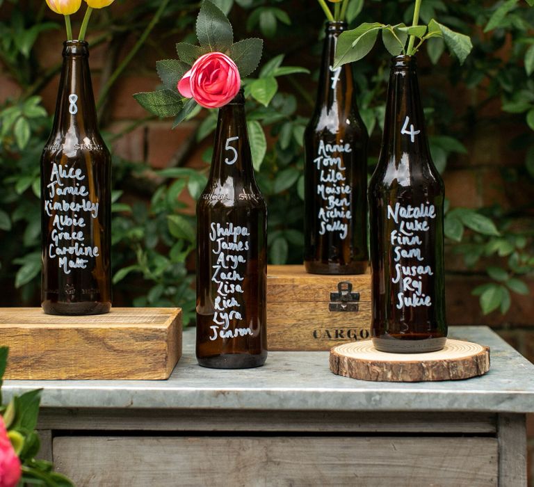 Bottle table plan for a rustic wedding, created using dark brown beer bottles, a white Pebeo pen, wooden crates and log slices, peonies and tulips.