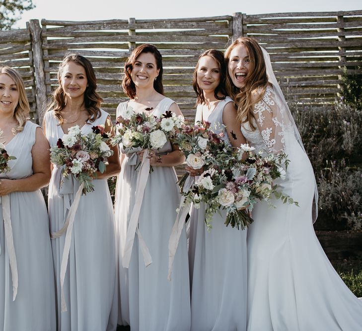 Bridal Party Portrait with Bridesmaids in Grey Dresses and Bride in Lace Wedding Dress Holding Their Widflower Bouquets