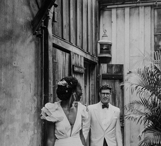 Stylish Bride in Secondhand Johanna Ortiz Wedding Dress with Ruffled Sleeves and Skirt and Groom in White Tuxedo Jacket and Bow Tie