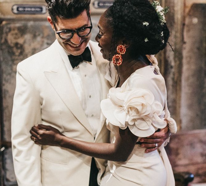 Stylish Bride in Johanna Ortiz Wedding Dress with Ruffled Shoulder Detail Embracing Her Groom in a White Tuxedo Jacket