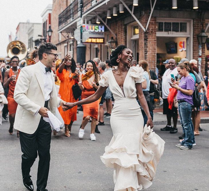 Stylish Bride and Groom Walking Down the StreetFollowed by A Brass Band Procession and Their Wedding Guests