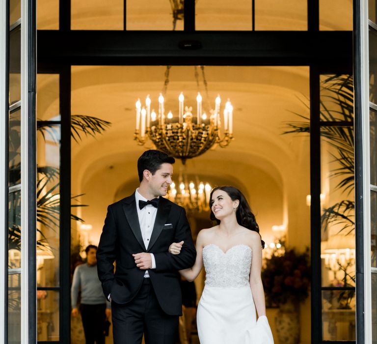 Glamorous Bride and Groom Arm in Arm Walking Out of Their Wedding Venue