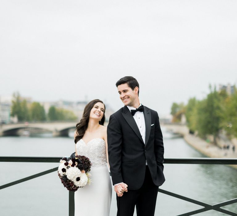 Bride in Tara Keely Wedding Dress and Groom in Black Tie Suit Posing in Front of the River Seine