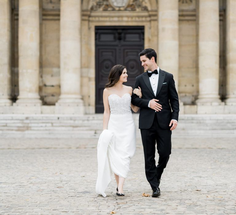 Bride in Off the Shoulder Tara Keely Wedding Dress and Groom in Black Tuxedo Hand in Hand Through the Streets of Paris