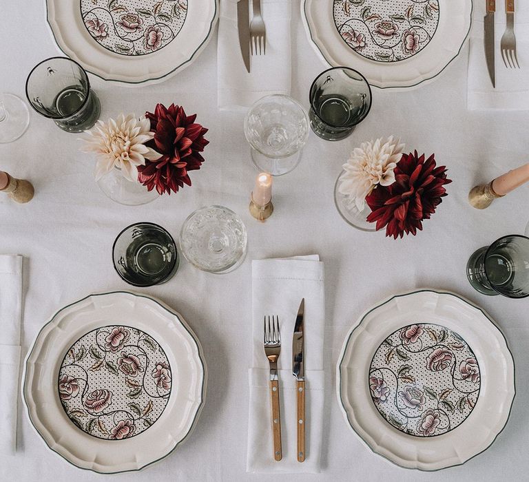 Intimate table setting with patterned tableware, candlesticks and bud vases.