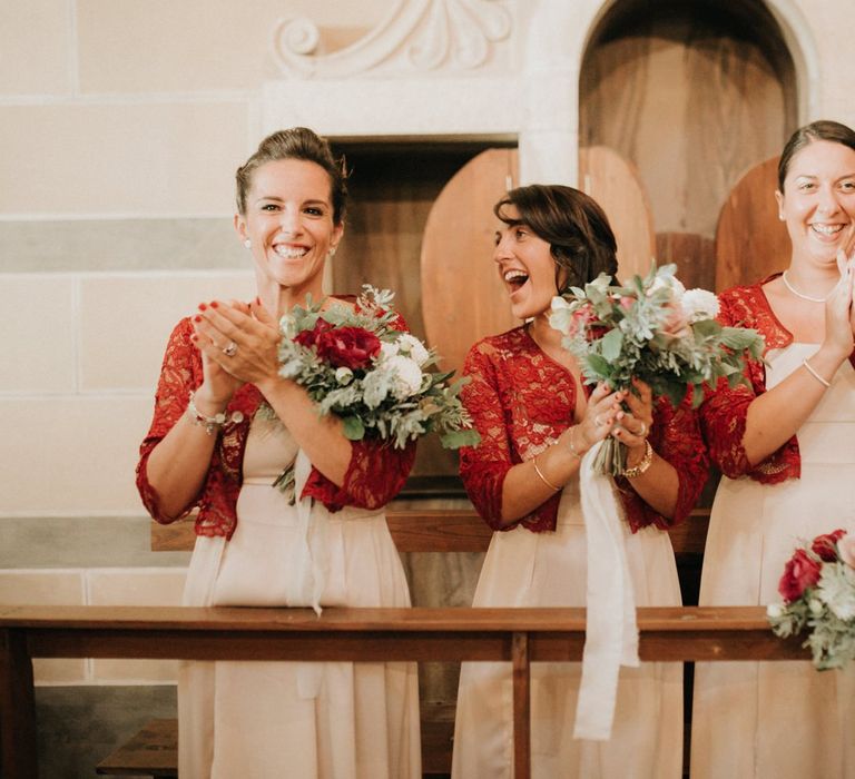 Bridesmaids in red lace cover-ups applaud bride and groom