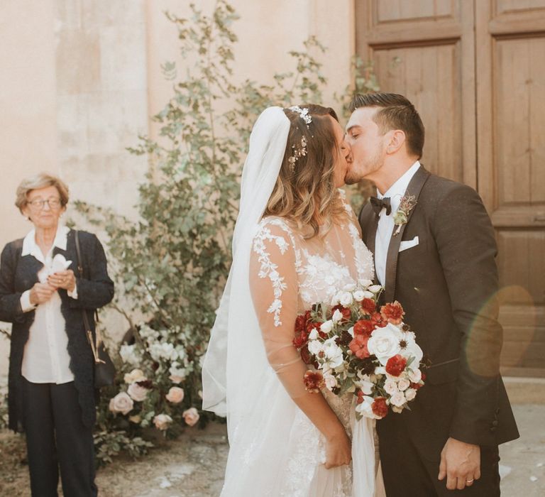 Bride and groom kiss after ceremony with blush and red bouquet