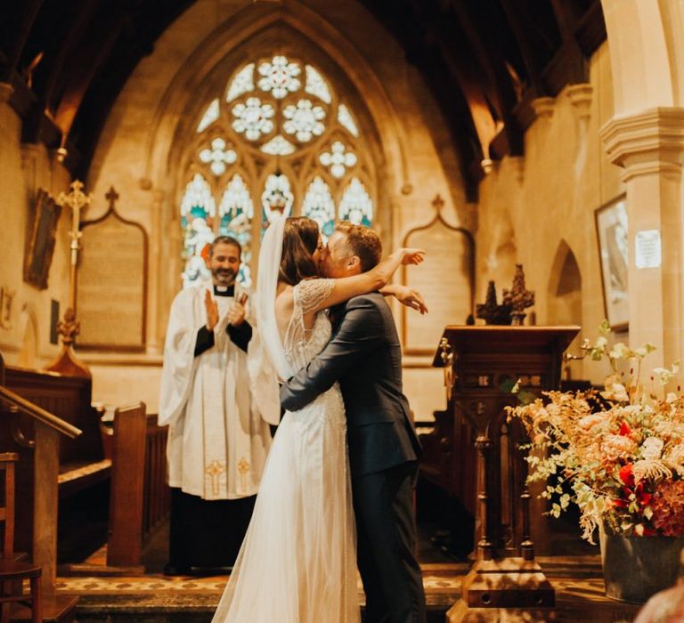 Bride in Maggie Sottero wedding dress and groom kiss at altar