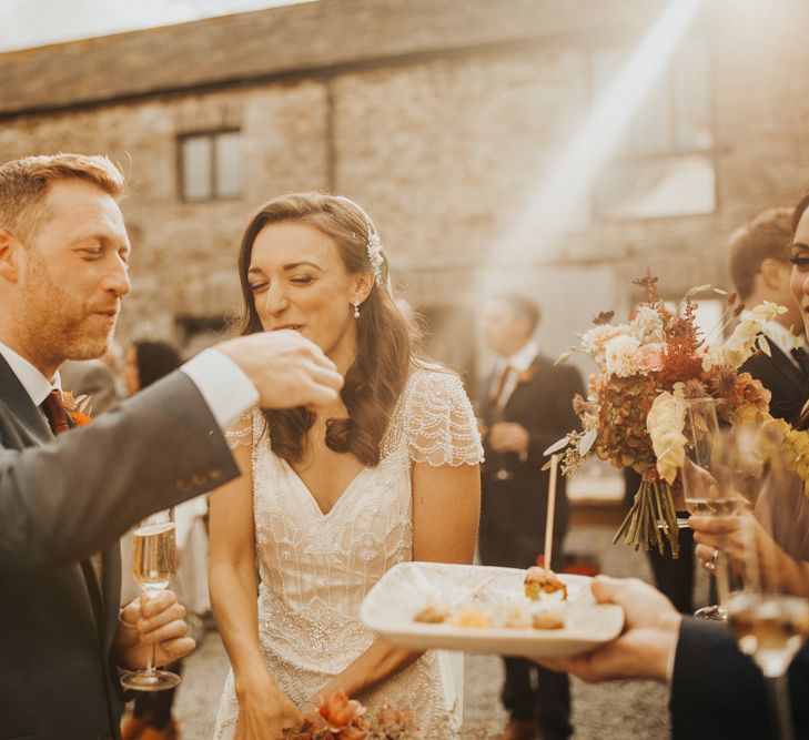 Bride in Maggie Sottero wedding dress with groom eating canapés