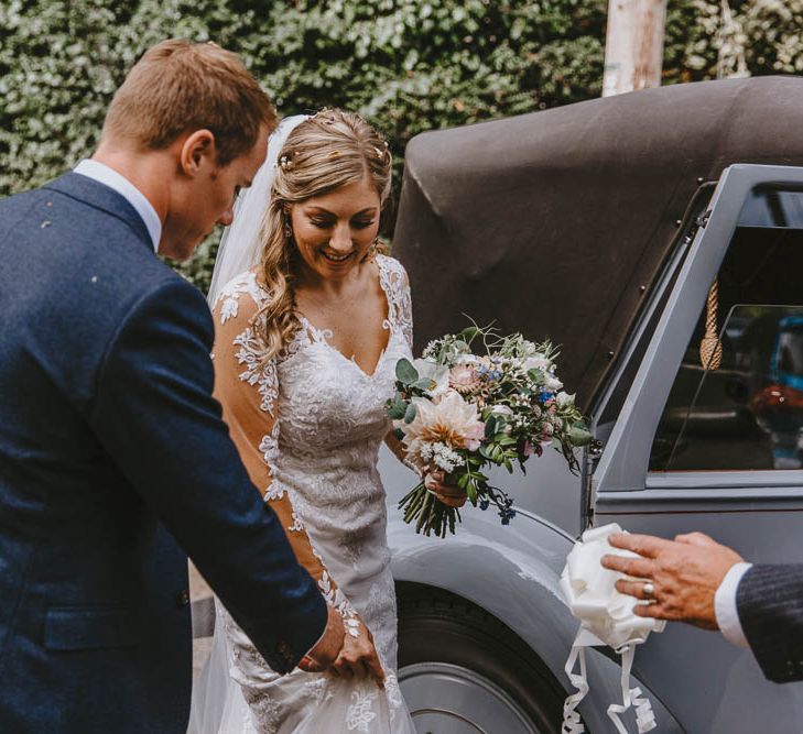 Groom in Blue Ted Baker Suit Helping His Bride in Lace Wedding Dress into the Vintage Wedding Car