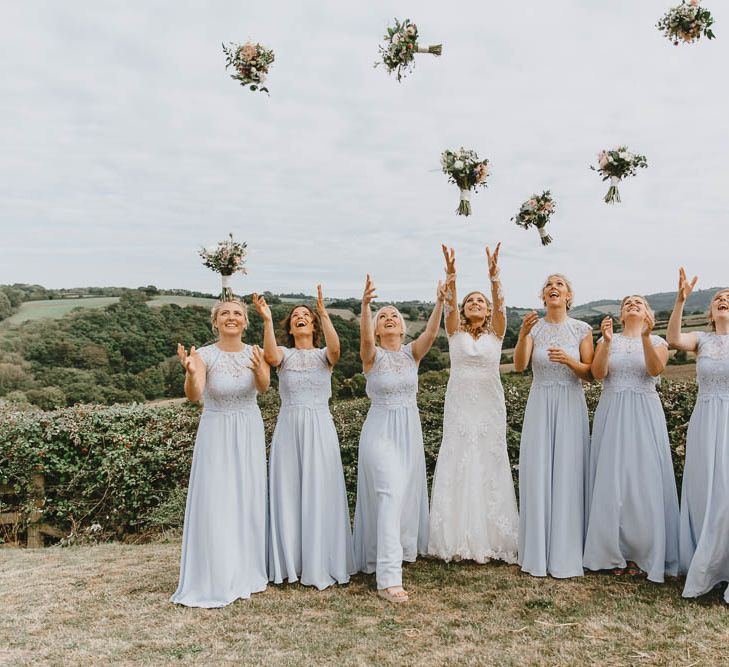 Bridal Party Portrait with Bridesmaids in Blue Lace Dresses and Bride in Longsleeve Sincerity Bridal Wedding Dress Throwing Their Bouquets in the Air