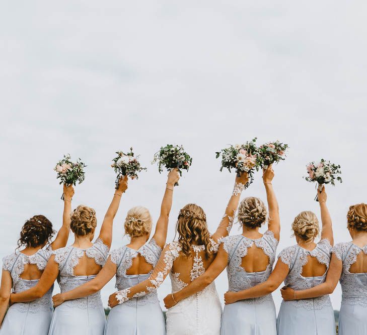 Bridal Party Portrait with Bridesmaids in Blue Lace Dresses and Bride in Longsleeve Sincerity Bridal Wedding Dress Holding Their Bouquets in the Air