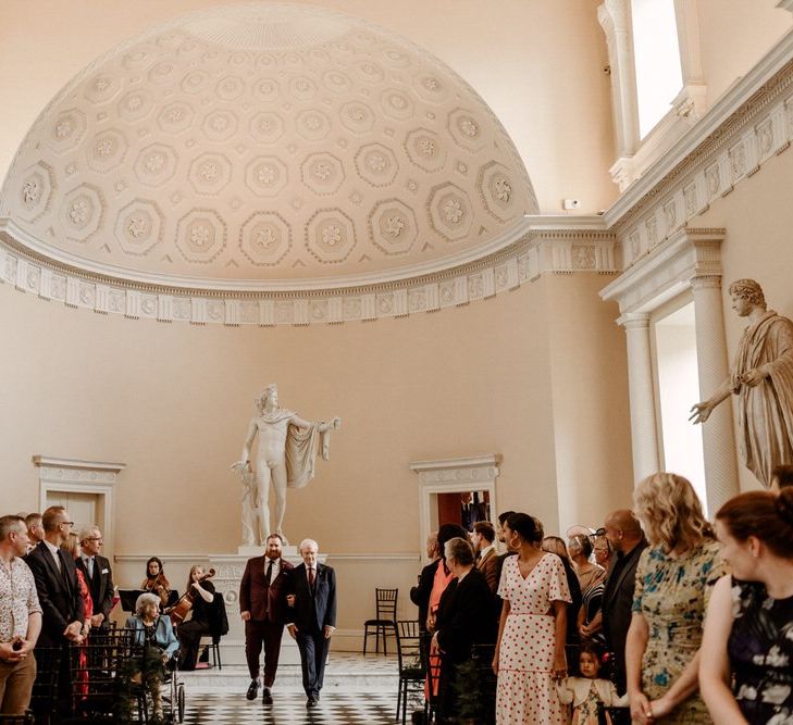 Groom in burgundy suit walking down the aisle with his father