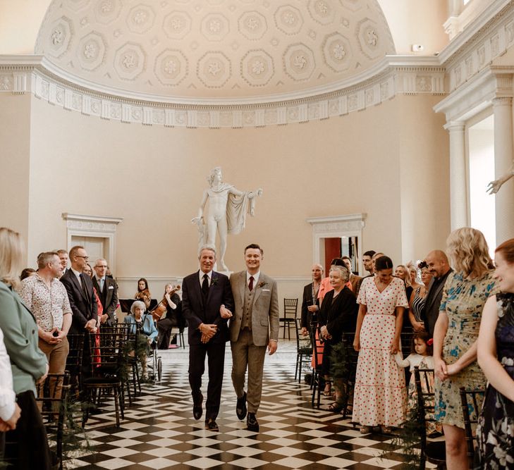 Groom in beige checked suit walking down the aisle with his father