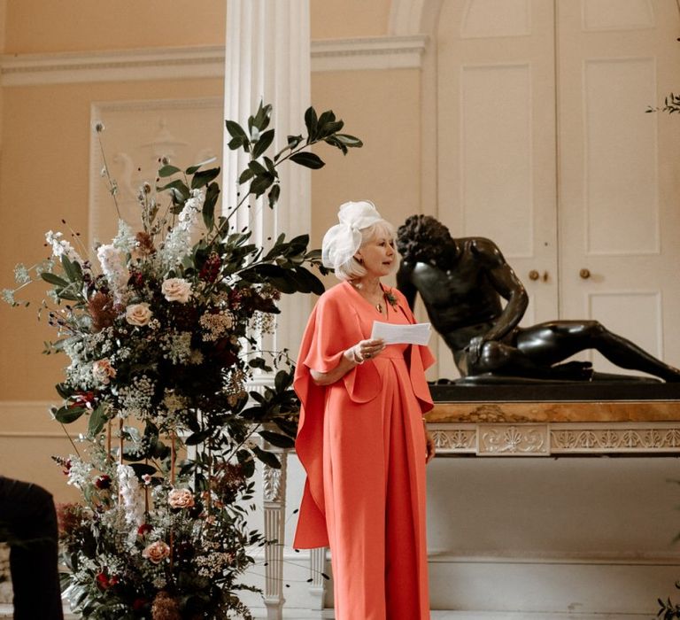 Mother of the groom in coral outfit performing a wedding reading