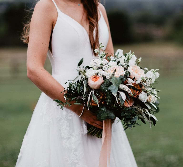 Bride holding a romantic peach and white flower bouquet with foliage and ribbon