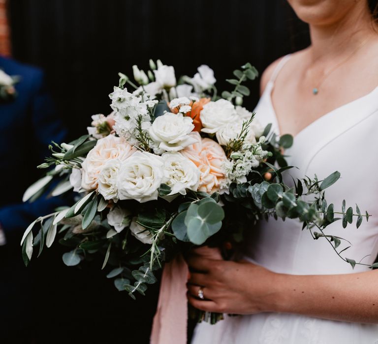 peach and white rose wedding bouquet tied with foliage and ribbon