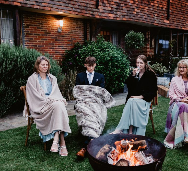 Wedding guests wrapped in blankets sat by the firepit